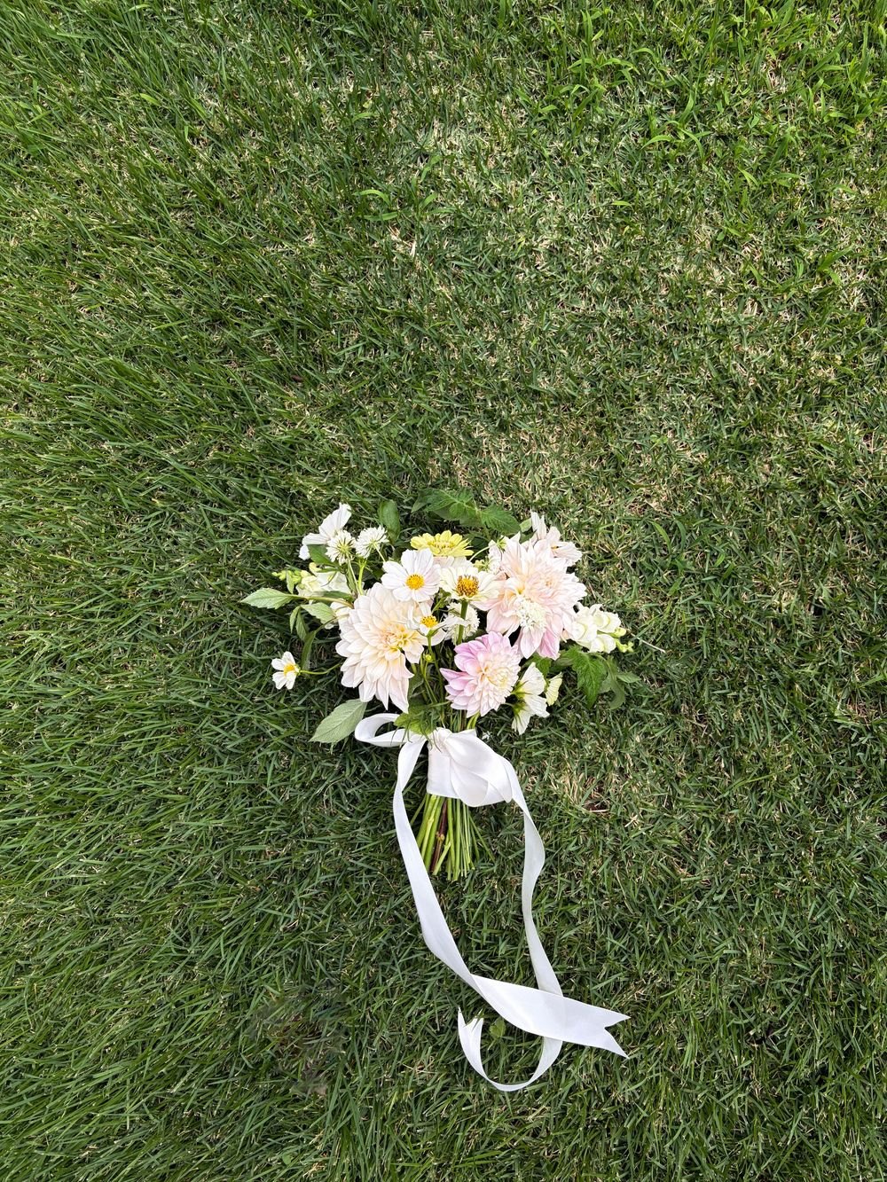 White bridal bouquet with ribbons resting on grass